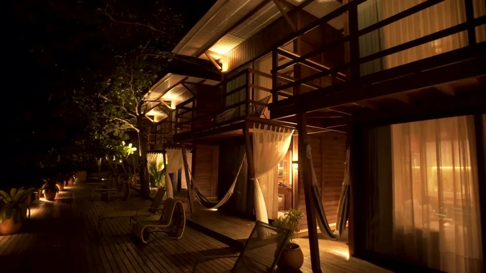 Lodges iluminados à noite, com redes nas varandas e o deck de madeira